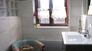 A bathroom with a window, a sink, a chair with towels, and a decorative item. - Le Bretzel Apartment with Mountain View and Wi-Fi (Ribeauvillé)