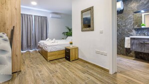 Een moderne slaapkamer met een houten bed, een nachtkastje met een bloevas, een spiegel aan de muur en een badkamer met een marmeren aanrecht.