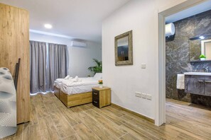 A modern bedroom with a wooden bed, a bedside table with a vase of flowers, a mirror on the wall, and a bathroom with a marble countertop. - Modern, Central 1BR Penthouse – Valletta View (Tal-Pietà)