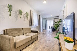 A living room with a sofa, a dining area with a table and chairs, and a kitchen area with a TV and potted plants. - Modern, Central 1BR Penthouse – Valletta View (Tal-Pietà)