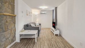 Una sala moderna con una pared de acento de piedra, un sofá gris, una mesa de centro blanca y un televisor de pantalla plana.