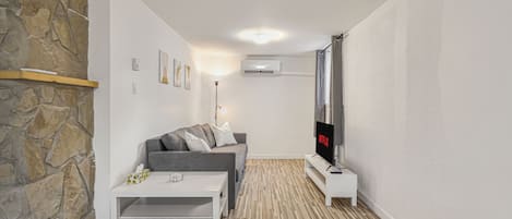 Uma sala de estar moderna com uma parede de destaque em pedra, um sofá cinza, uma mesa de centro branca e uma televisão de tela plana.