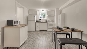 Cocina compacta con armarios blancos, microondas, refrigerador y una mesa de comedor lista para dos.