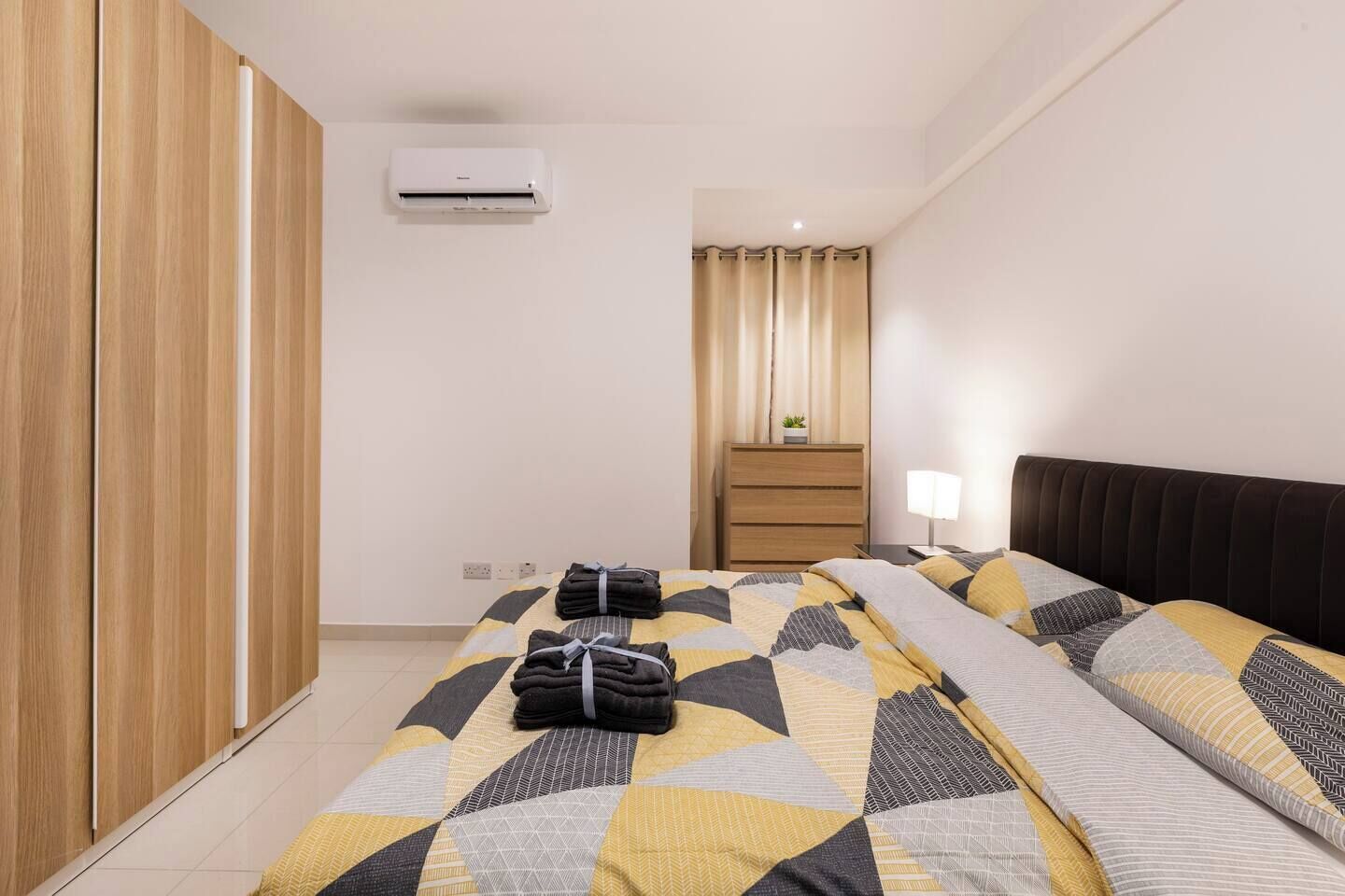 Una habitación de hotel con una cama, una mesita de noche, una lámpara, un armario y un equipo de aire acondicionado.