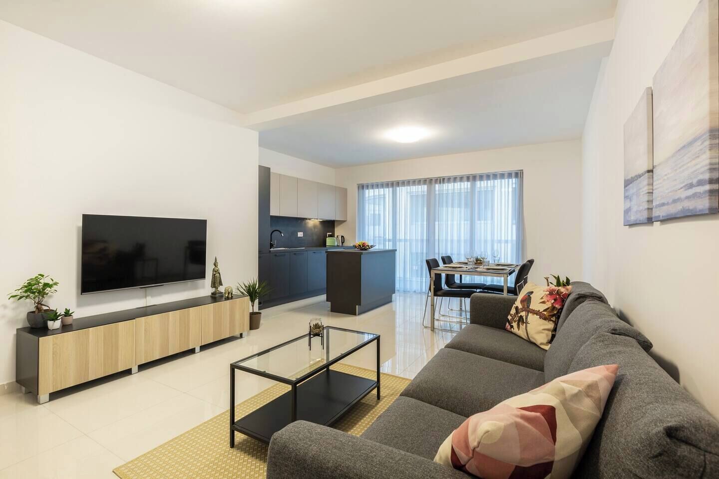 Una sala de estar moderna con un televisor de pantalla plana, un sofá, una mesa de centro y un comedor con una mesa y sillas.