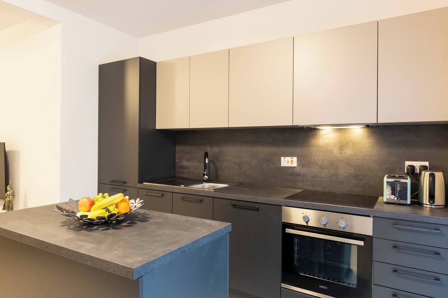 Una cucina moderna con forno integrato, lavello e una ciotola di frutta sul piano di lavoro.