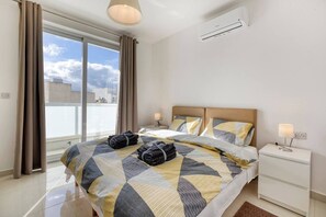 Ein Hotelzimmer mit einem großen Bett, einem Nachttisch mit Lampe, einem Fenster mit Vorhängen und einer Klimaanlage.
