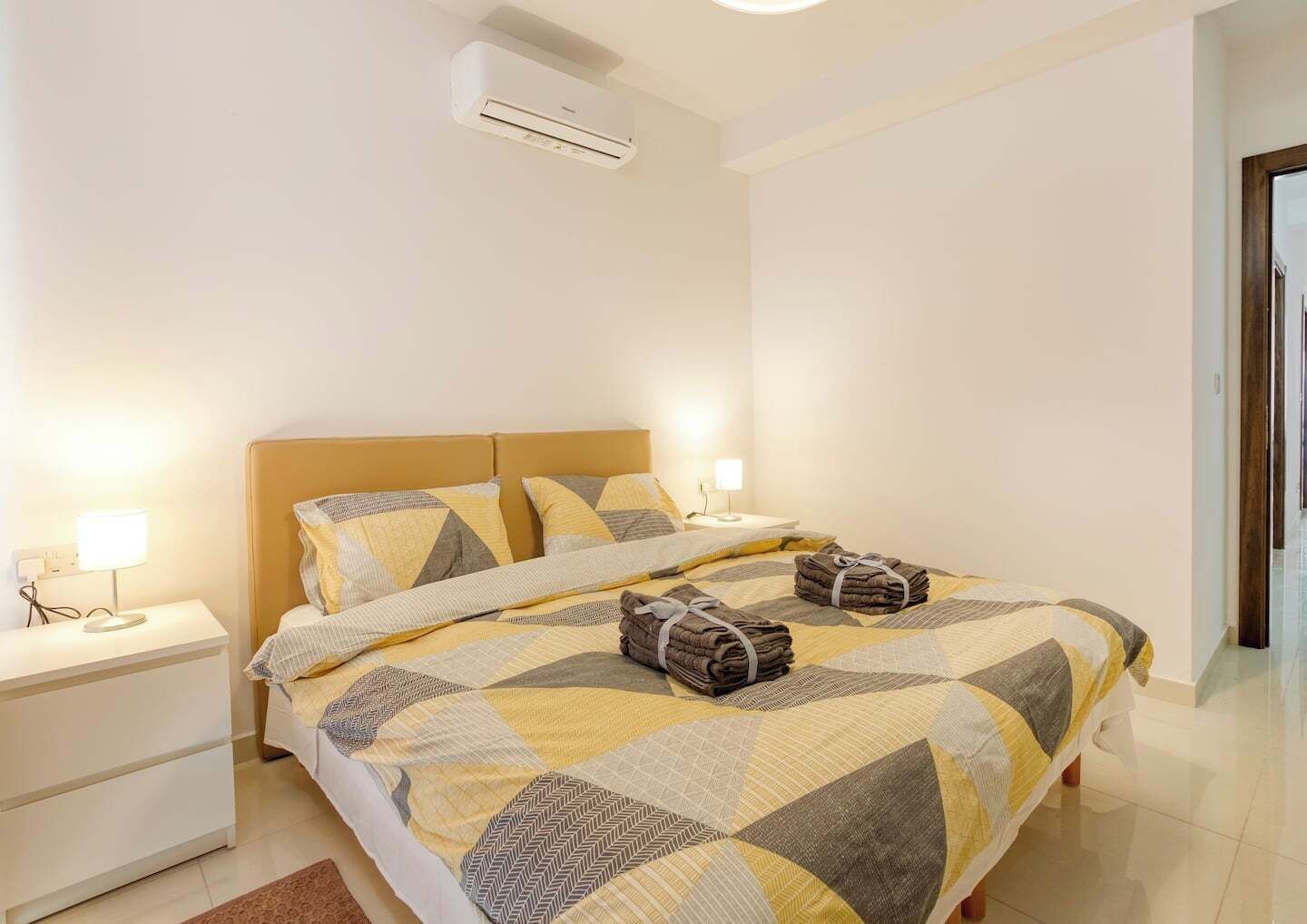 Una camera d'albergo con un letto, comodini, una lampada e un condizionatore d'aria.