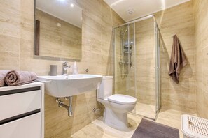 Ein modernes Badezimmer mit einer gläsernen Duschkabine, einem weißen Waschbecken und einer Toilette.