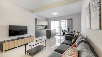 Un soggiorno moderno con televisione a schermo piatto, un tavolino in vetro e un divano grigio con cuscini decorativi.