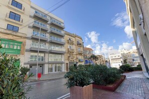 Ein mehrgeschossiges Wohngebäude mit Balkonen, eine Straße davor und ein klarer Himmel.
