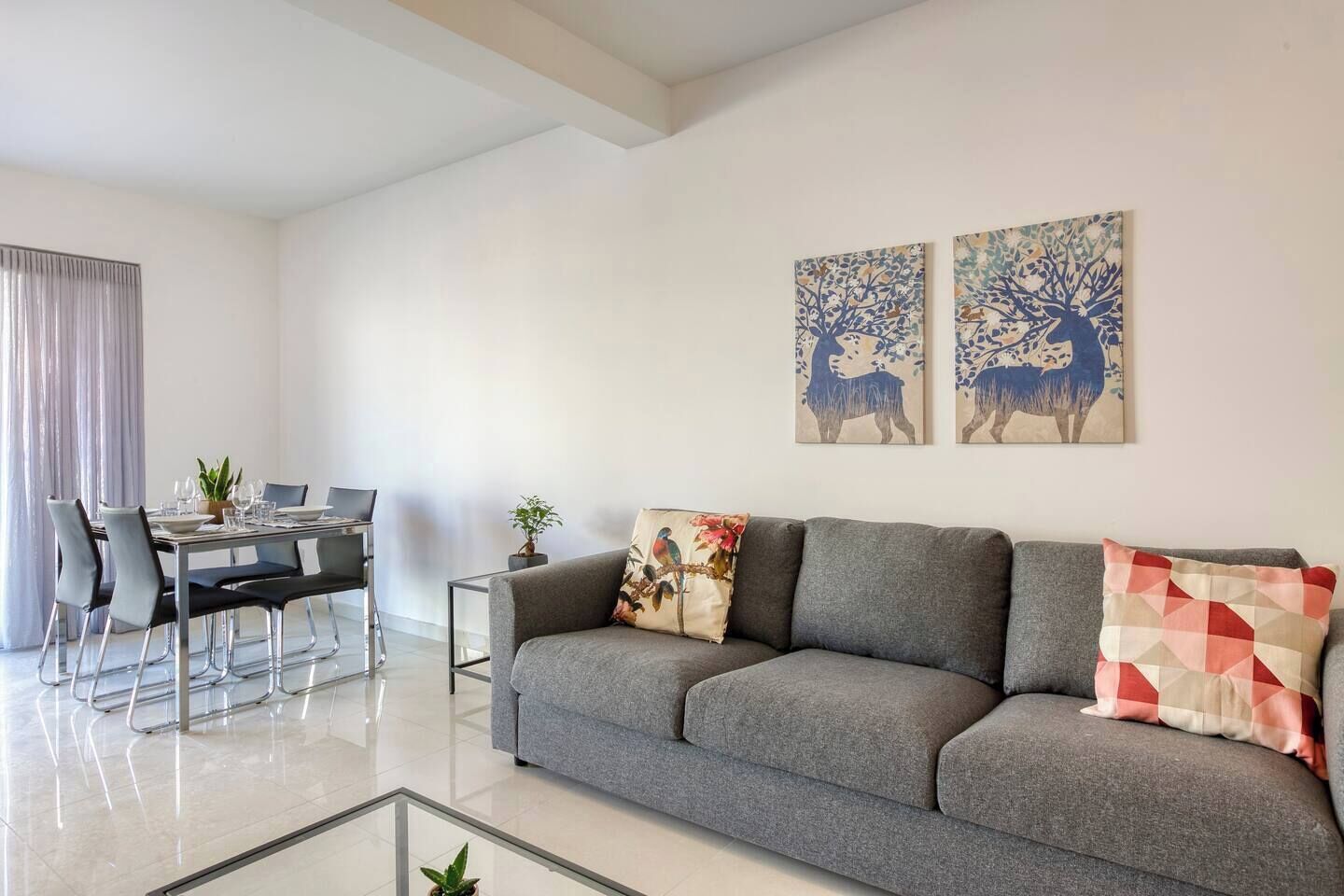 Una sala moderna con un sofá gris, una mesa de comedor con sillas y dos cuadros colgados en la pared.