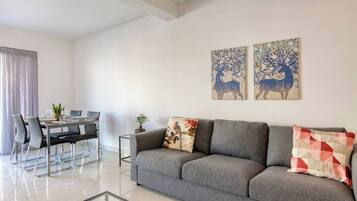 Una sala moderna con un sofá gris, una mesa de comedor con sillas y dos cuadros colgados en la pared.