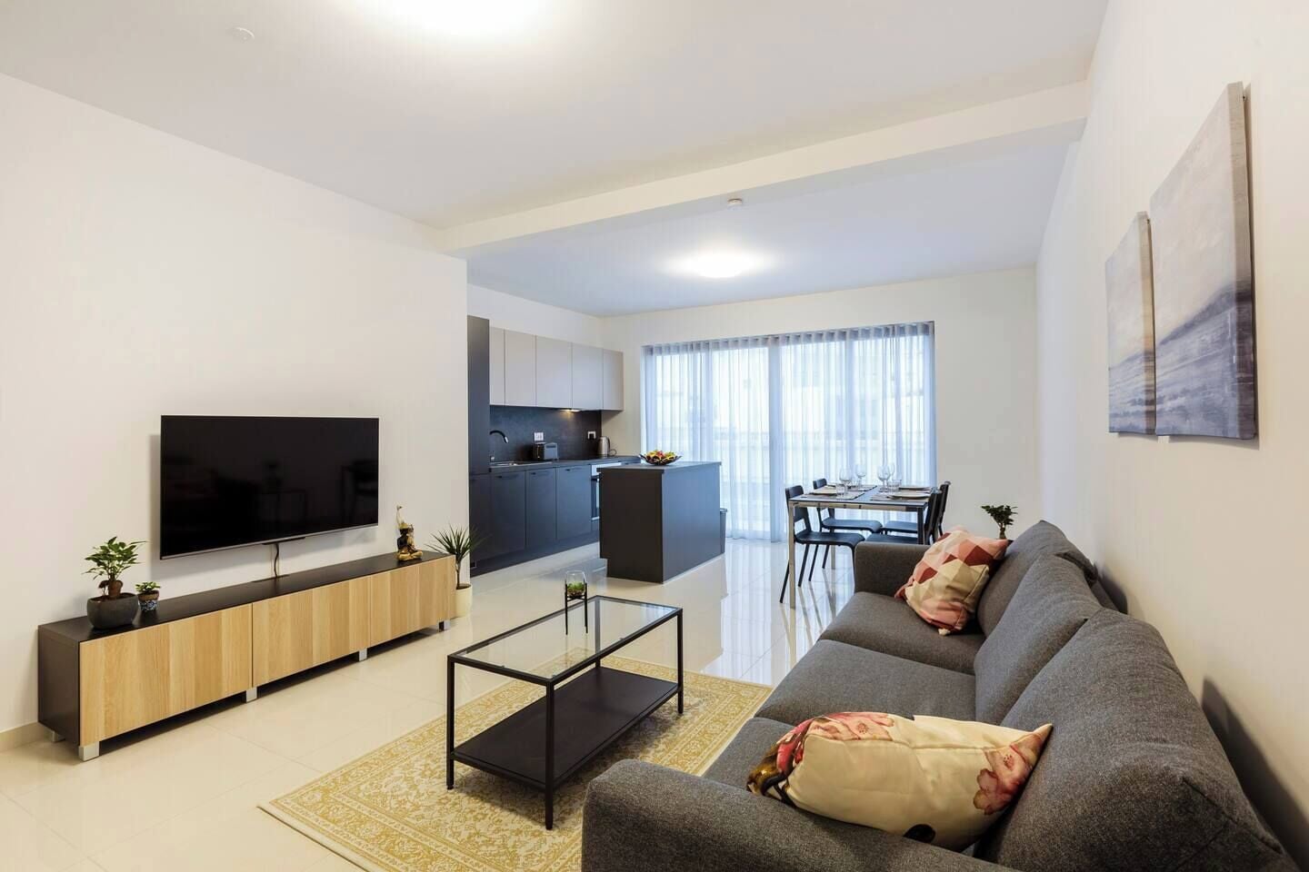 Ein modernes Wohnzimmer mit Flachbildfernseher, Sofa, Couchtisch und einem Essbereich mit Tisch und Stühlen.