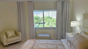 Une chambre à coucher comprenant un lit, un banc, une chaise, une table de chevet avec une lampe et une fenêtre avec des rideaux.