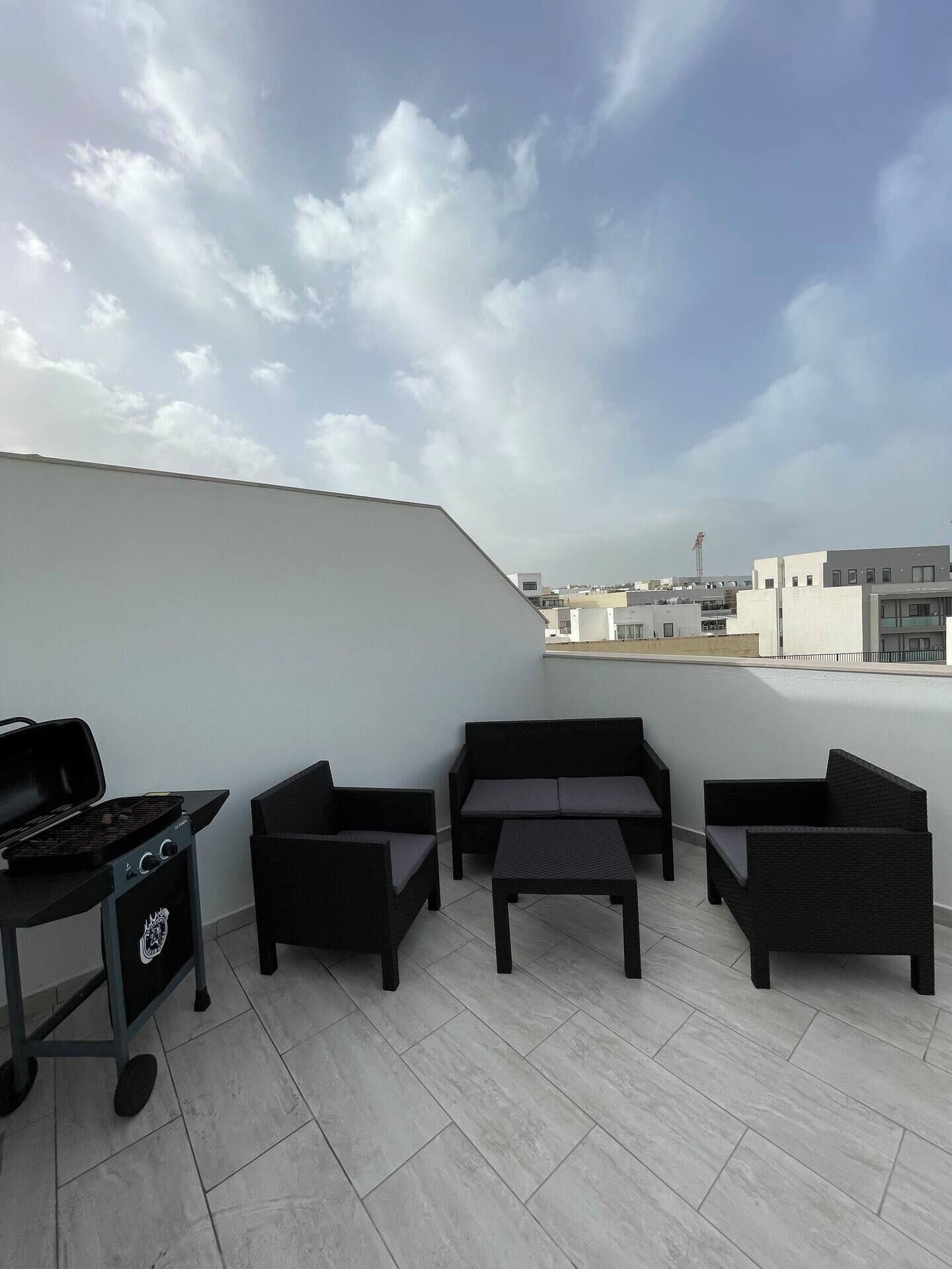 Eine Dachterrasse mit Grill, Sitzgelegenheit und Blick auf die Skyline der Stadt.