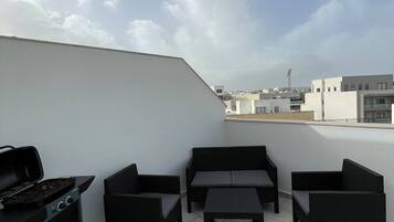 Eine Dachterrasse mit Grill, Sitzgelegenheit und Blick auf die Skyline der Stadt.