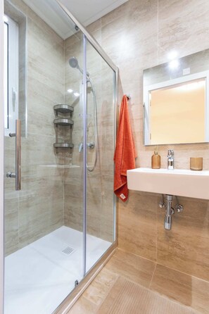 Ein modernes Badezimmer mit einer ein Glasfach werenden Dusche, einem weißen Waschbecken und einem Spiegel darüber.