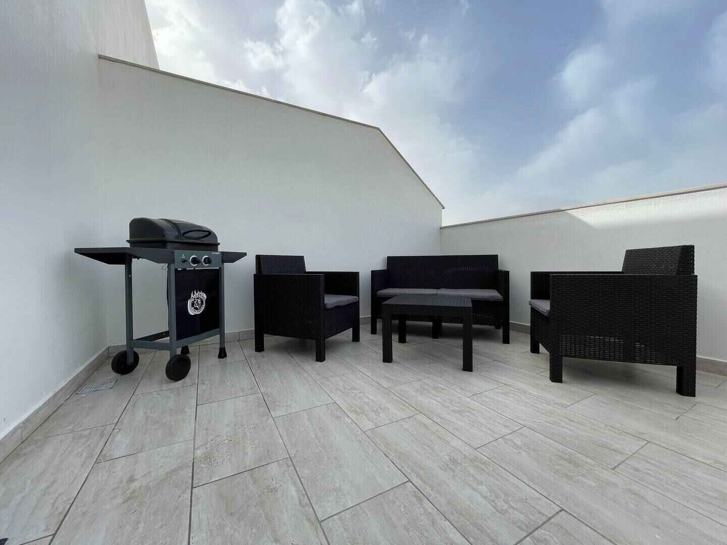 Una terrazza sul tetto con barbecue, mobili in vimini e cielo sereno.