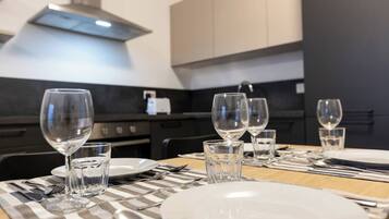 Una mesa de comedor dispuesta con platos, vasos y cubiertos, con una cocina moderna al fondo.