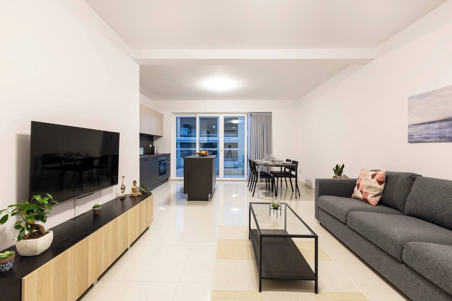 Una sala de estar moderna con un televisor de pantalla plana, un sofá, una mesa de centro y un comedor con mesa y sillas.