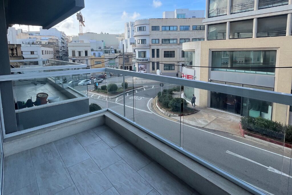 A balcony with a view of a city street, modern buildings, and a clear sky.