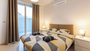 Une chambre d’hôtel comprenant un lit, deux tables de chevet, un appareil de climatisation et une fenêtre avec des rideaux.