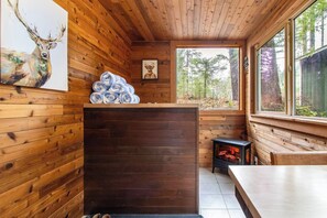 Ein Blockhaus-Interieur mit Holzwänden, Kamin, Essbereich und Fenster mit Blick auf einen Wald.
