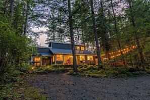 A two-story cabin with a deck, surrounded by dense forest. - Harry's Hideaway | Hot Tub | Fire pit | Mt Rainier (Packwood)