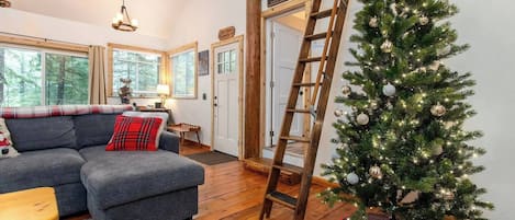 A cozy living room with a grey sofa, a Christmas tree, and a wooden ladder.