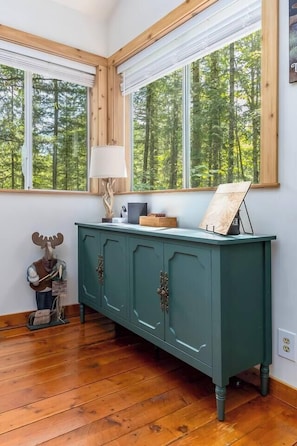 A room with a wooden floor, a green cabinet with two doors, a lamp, and a framed picture on top. - Harry's Hideaway | Hot Tub | Fire pit | Mt Rainier (Packwood)