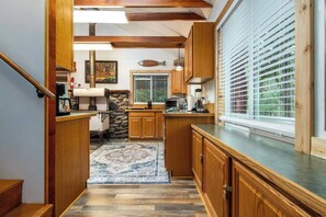 A kitchen with wooden cabinets, a stone fireplace, and a view of the outdoors. - Harry's Hideaway | Hot Tub | Fire pit | Mt Rainier (Packwood)