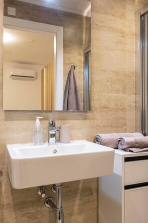 Un bagno con un lavandino bianco, uno specchio, un asciugamano e una bottiglia di sapone per le mani.