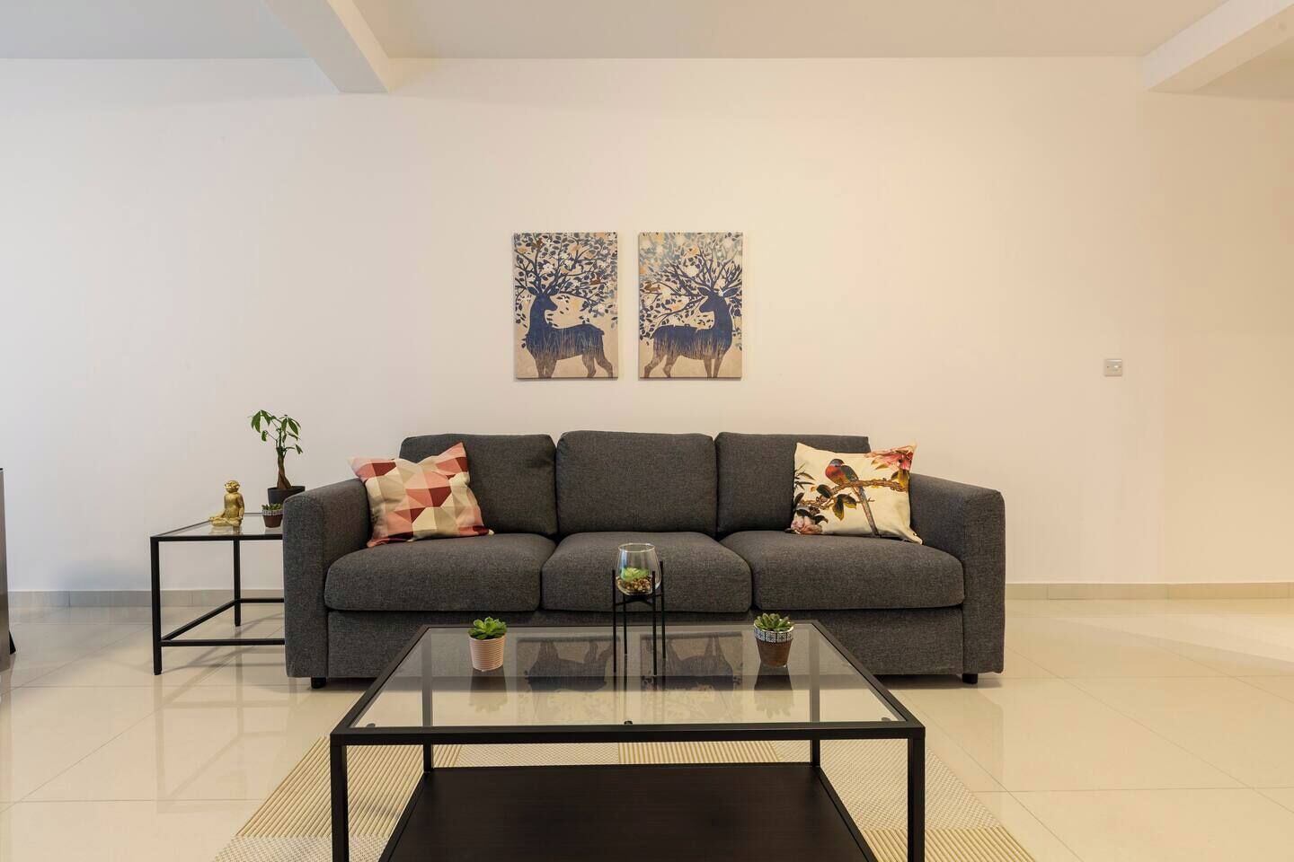 Un salon moderne avec un canapé gris, deux tables d’appoint et une table basse en verre.