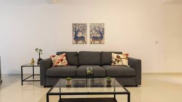 Un salon moderne avec un canapé gris, deux tables d’appoint et une table basse en verre.
