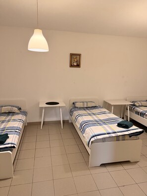 Un dormitorio con dos camas, una mesita pequeña, una lámpara colgante y un cuadro en la pared.