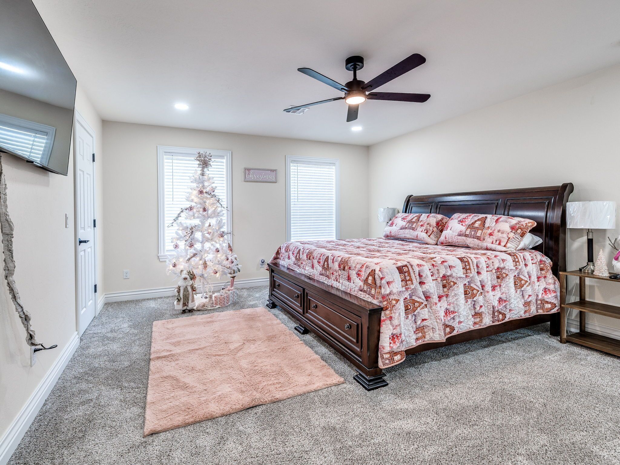 A bedroom with a bed, a ceiling fan, a Christmas tree, and a rug.