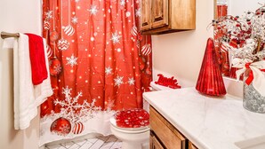 Un baño con cortina de ducha roja con motivos de copos de nieve, un inodoro blanco y un armario de madera sobre el lavamanos.