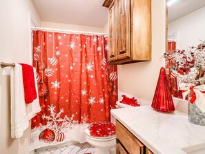 A bathroom with a red shower curtain featuring snowflake patterns, a white toilet, and a wooden cabinet above the sink. - Chickasha ChristmasTown - Family Holiday Retreat (Chickasha)