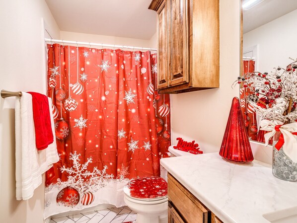 A bathroom with a red shower curtain featuring snowflake patterns, a white toilet, and a wooden cabinet above the sink.