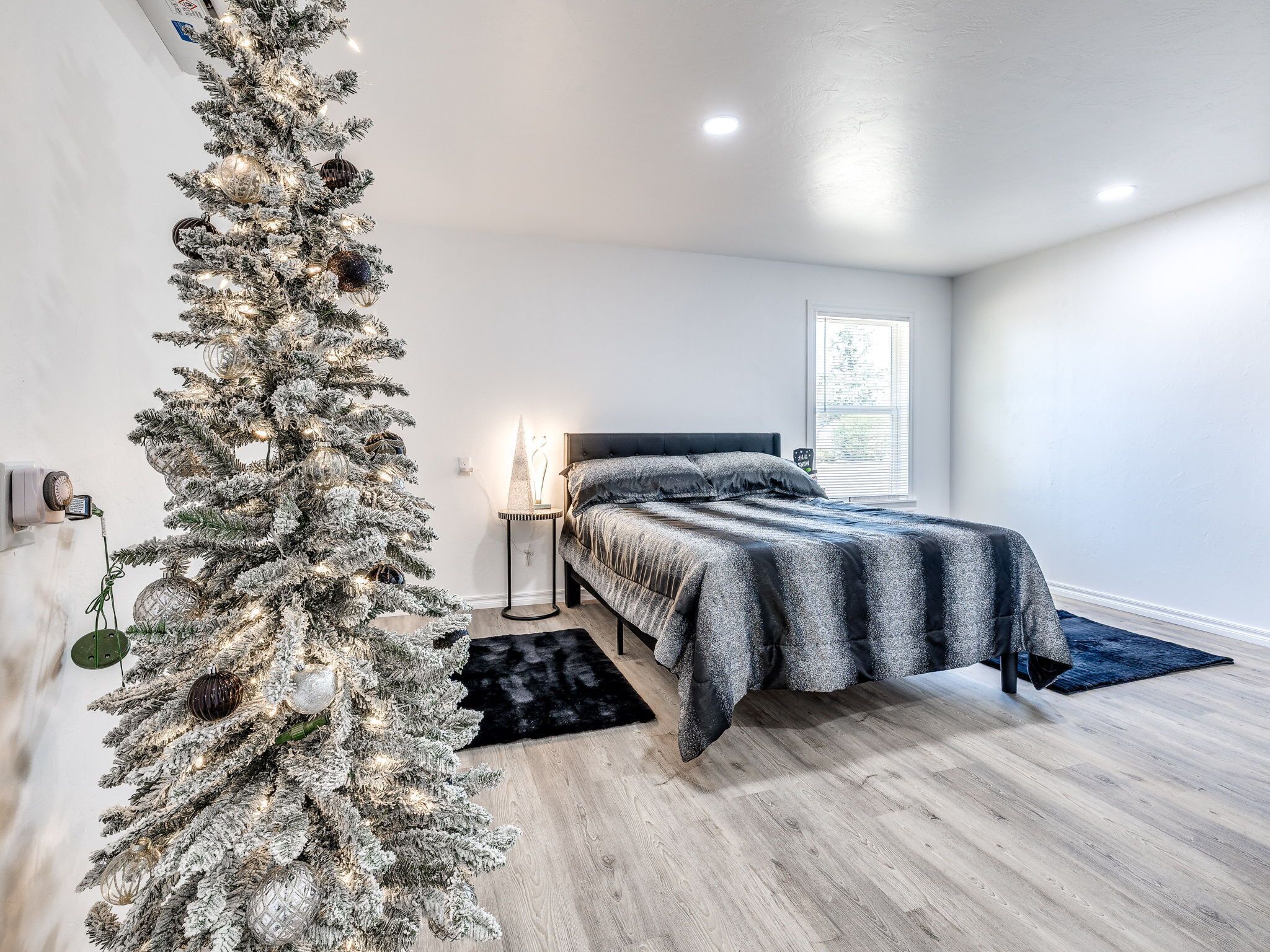 A bedroom with a bed, a nightstand, a Christmas tree, and a window.