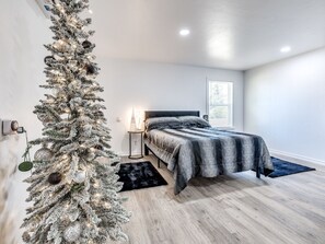 A bedroom with a bed, a nightstand, a Christmas tree, and a window.