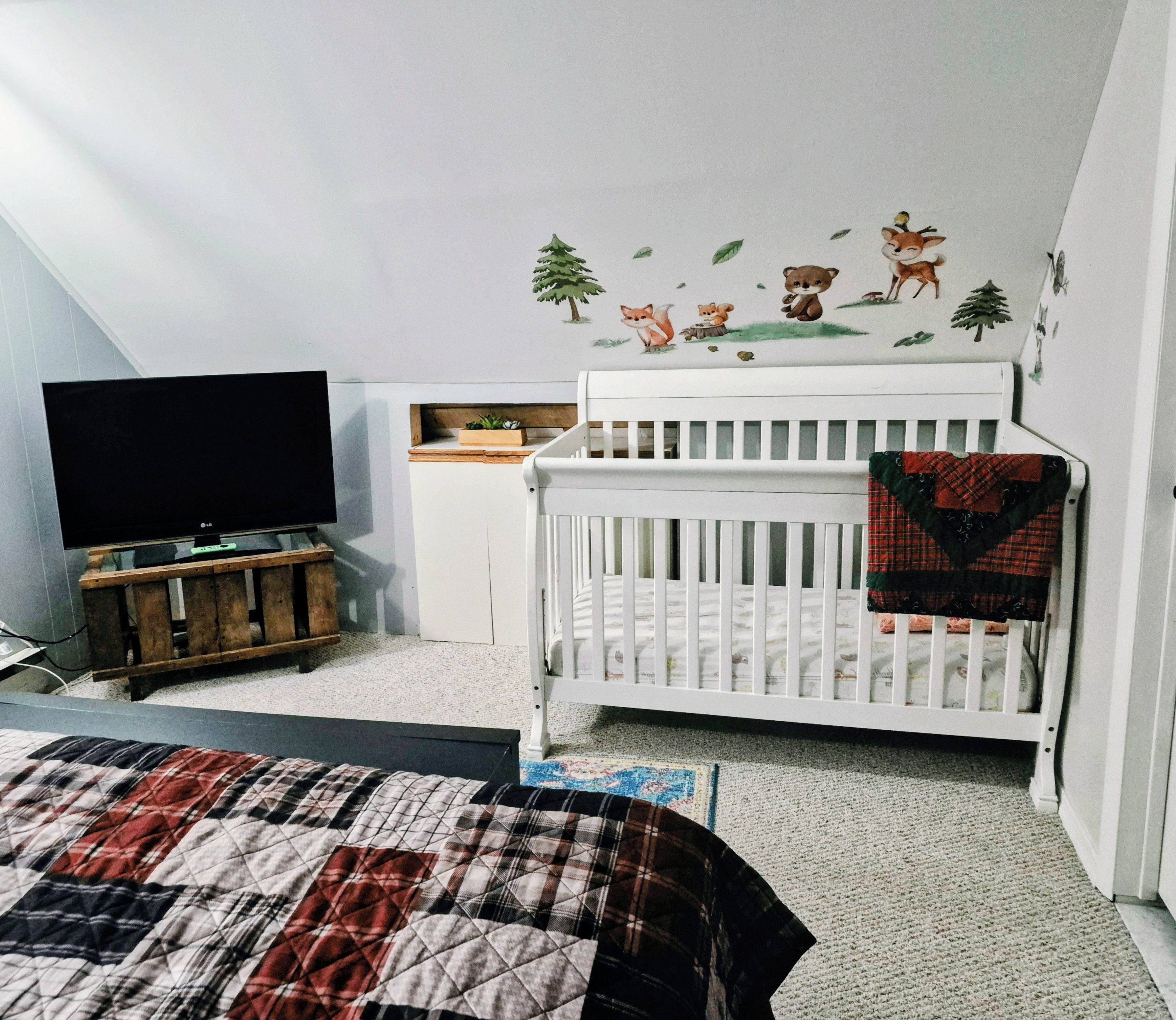 A bedroom with a crib, a television, and a wall decal.