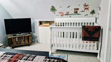 A bedroom with a crib, a television, and a wall decal.