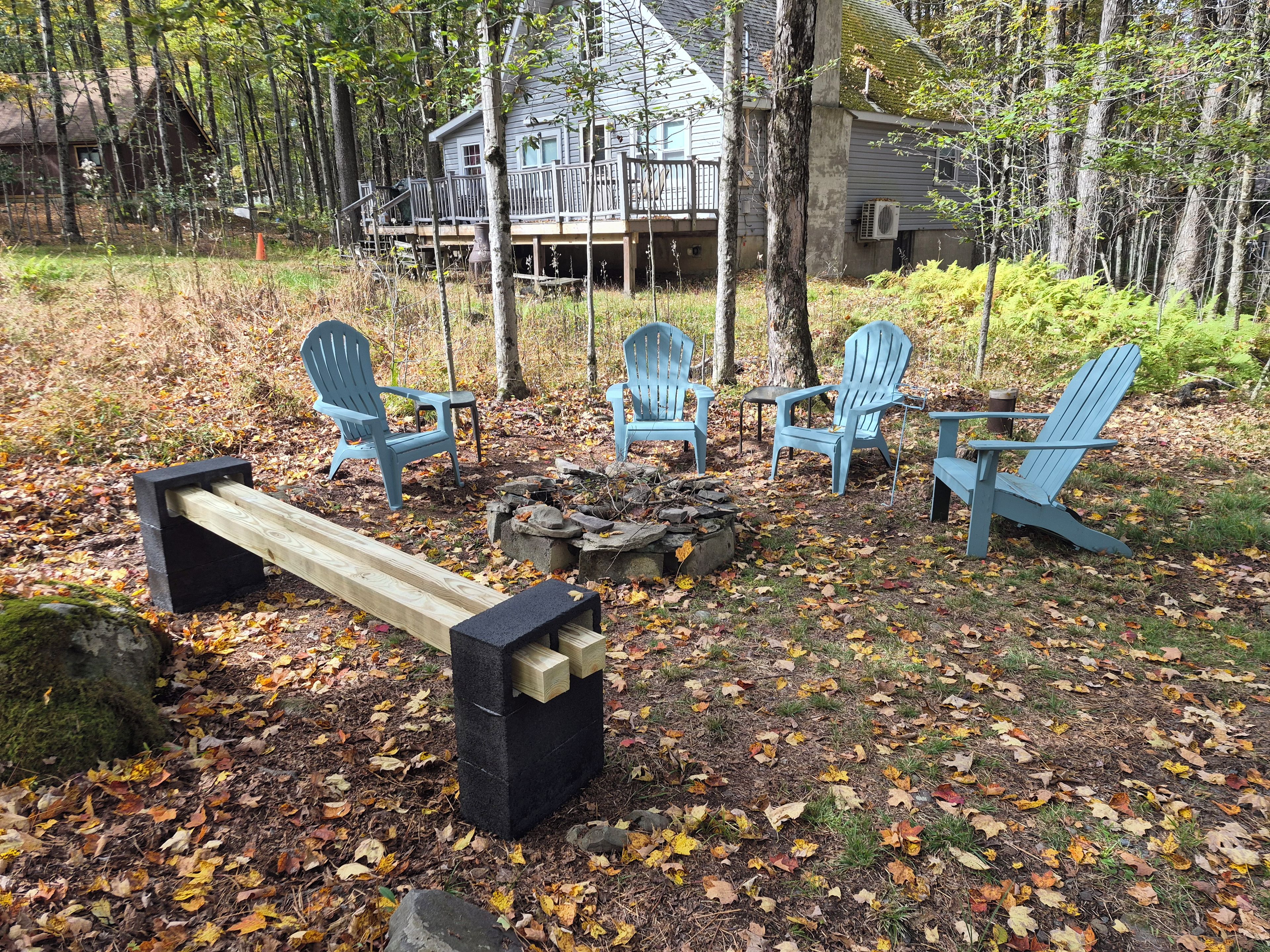 A wooden deck with Adirondack chairs and a fire pit in a forested area.
