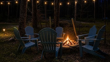Ein Lagerfeuer mit vier Adirondack-Stühlen, die darum herum in einer bewaldeten Gegend angeordnet sind.