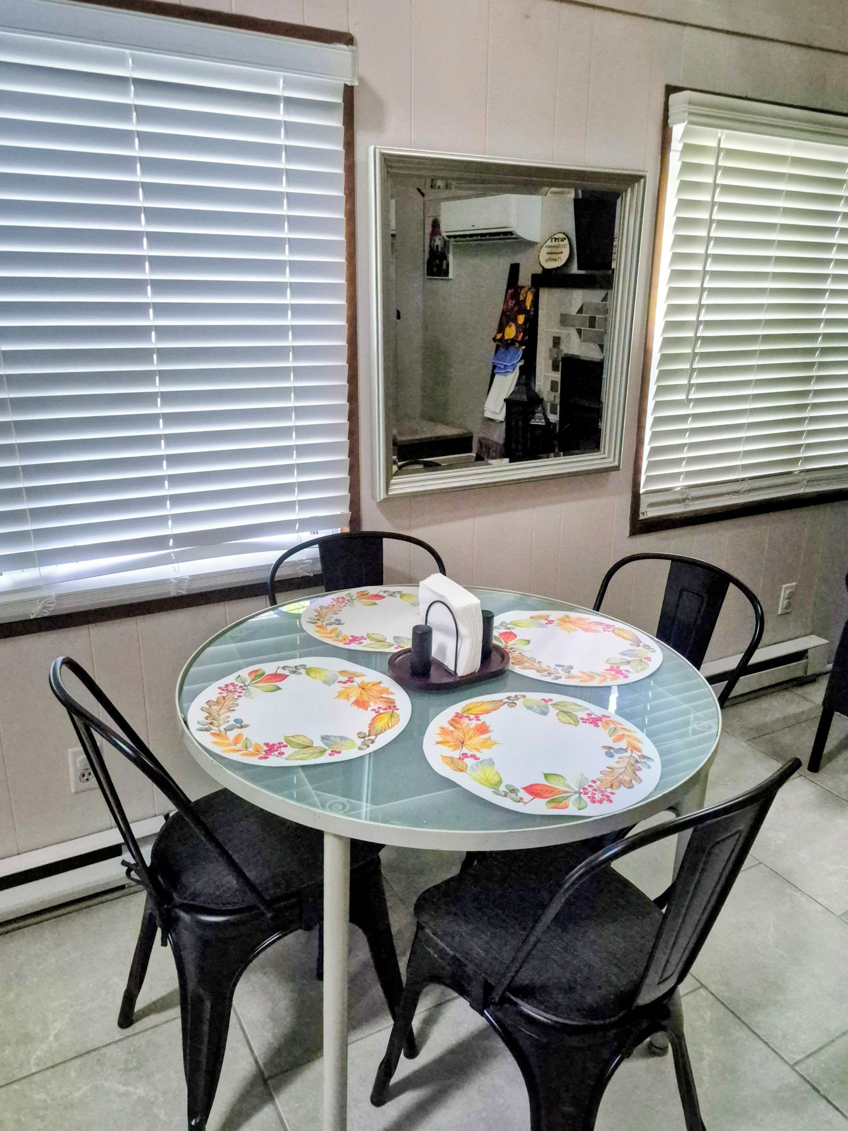 A dining area with a round table, four chairs, and a mirror on the wall.