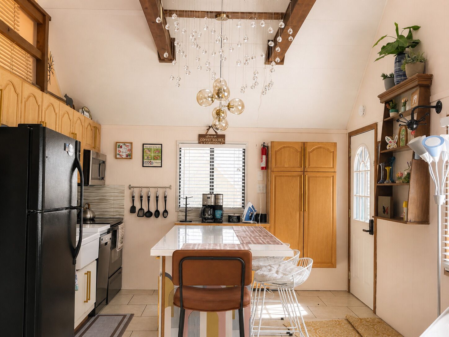 A kitchen with a black refrigerator, wooden cabinets, a dining table with chairs, hanging kitchen utensils, and a chandelier.