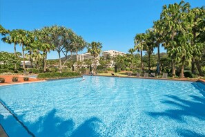 Una grande piscina con lettini e palme, circondata da edifici.