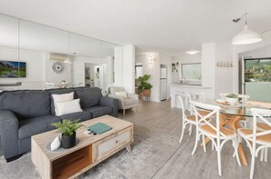 Un soggiorno moderno con un divano grigio, un tavolino da caffè con una pianta e un'area pranzo con sedie bianche e un tavolo in vetro.